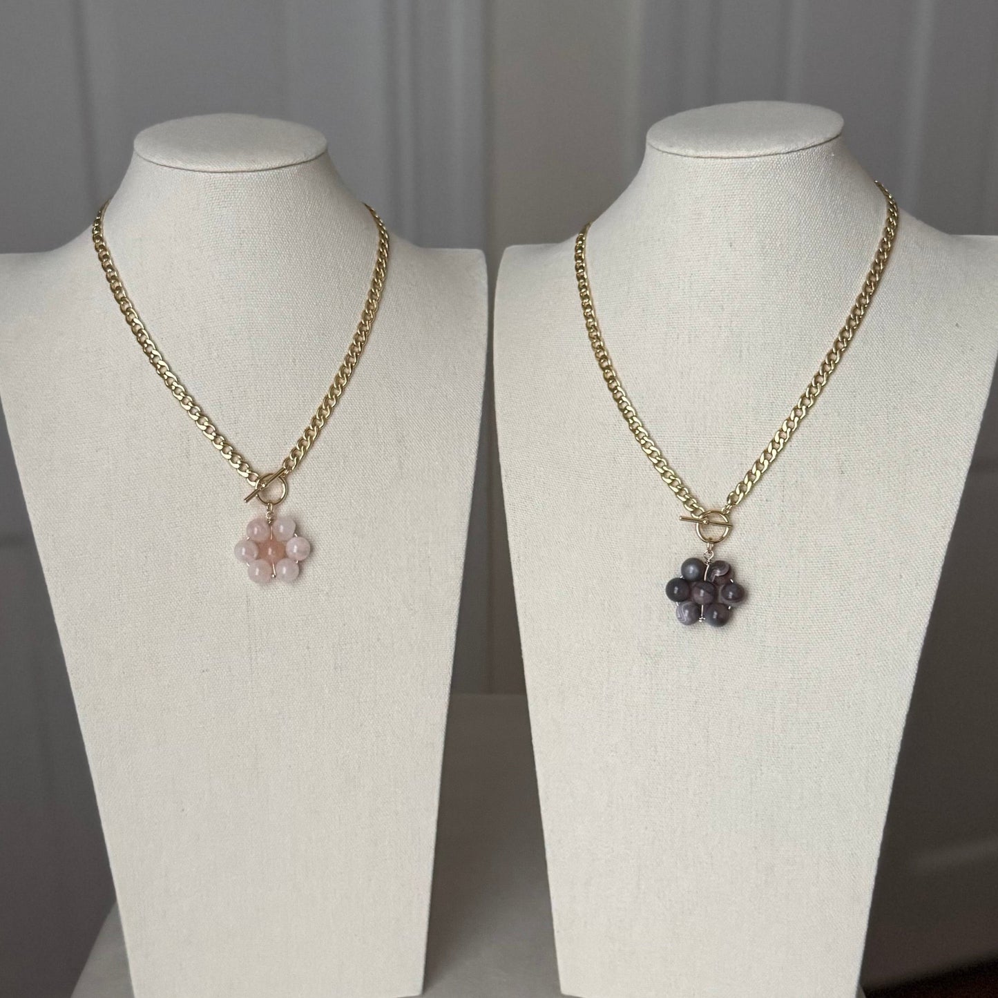 Two toggle necklaces with floral pendant on mannequin busts against a neutral background
