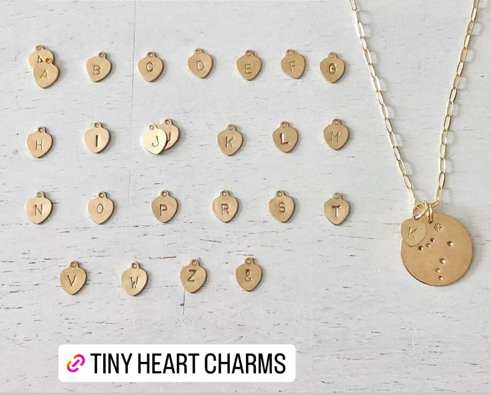 Gold tiny heart-shaped charms with a necklace on a light wooden background, featuring the brand 'Tiny Heart Charms'.