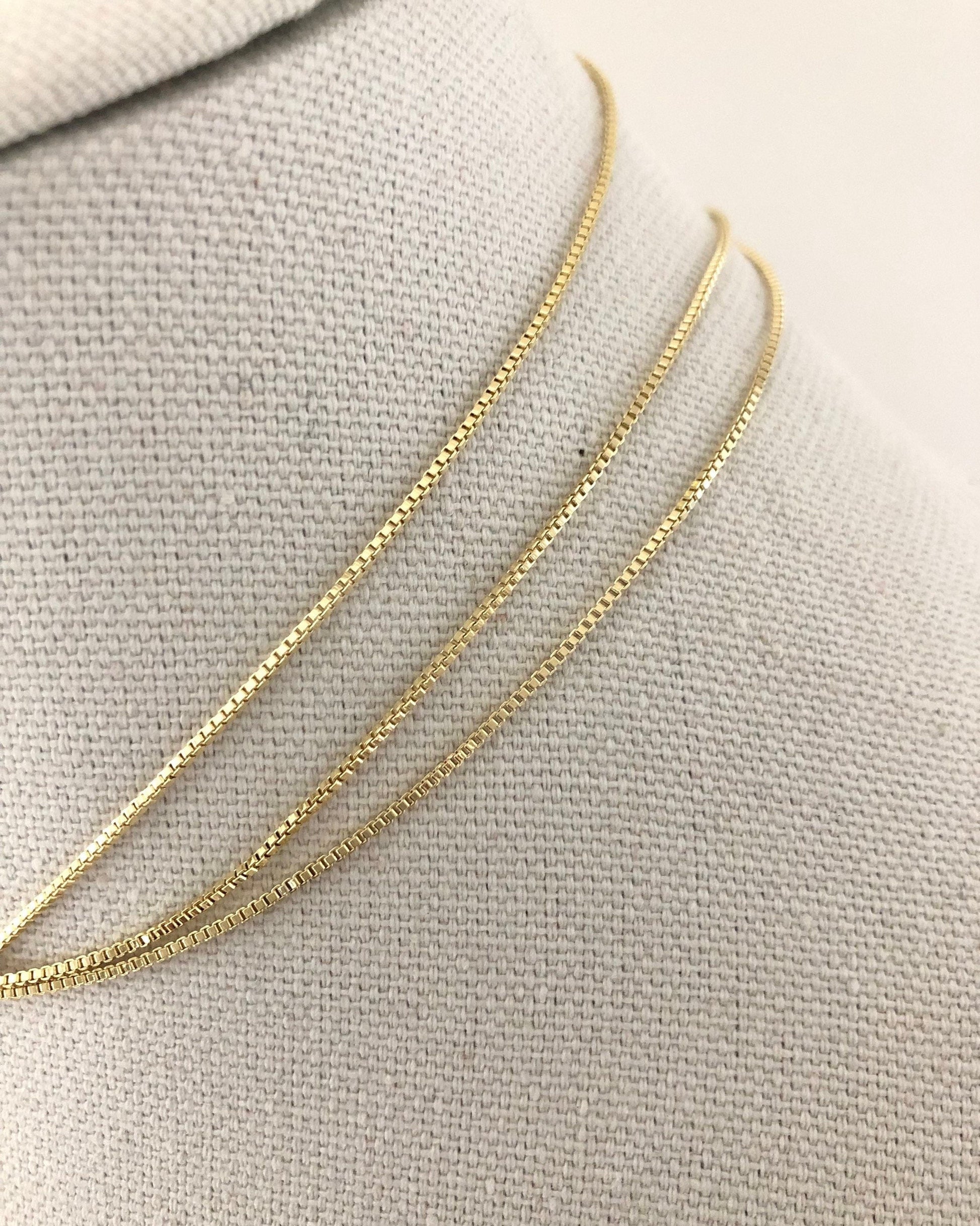 Gold box chain necklace on a light gray fabric background
