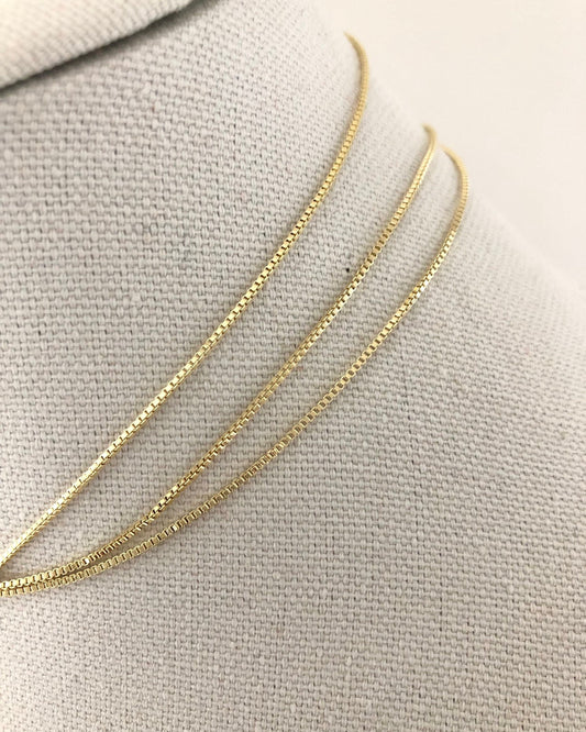 Gold box chain necklace on a light gray fabric background