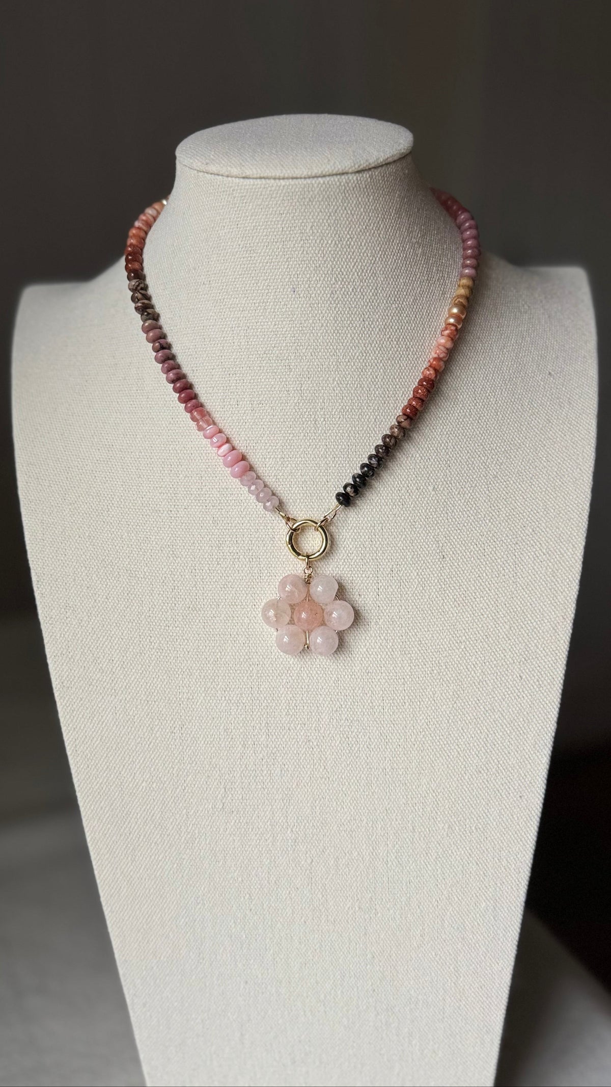 Necklace with a floral pendant on ombré necklace on a display bust against a dark background