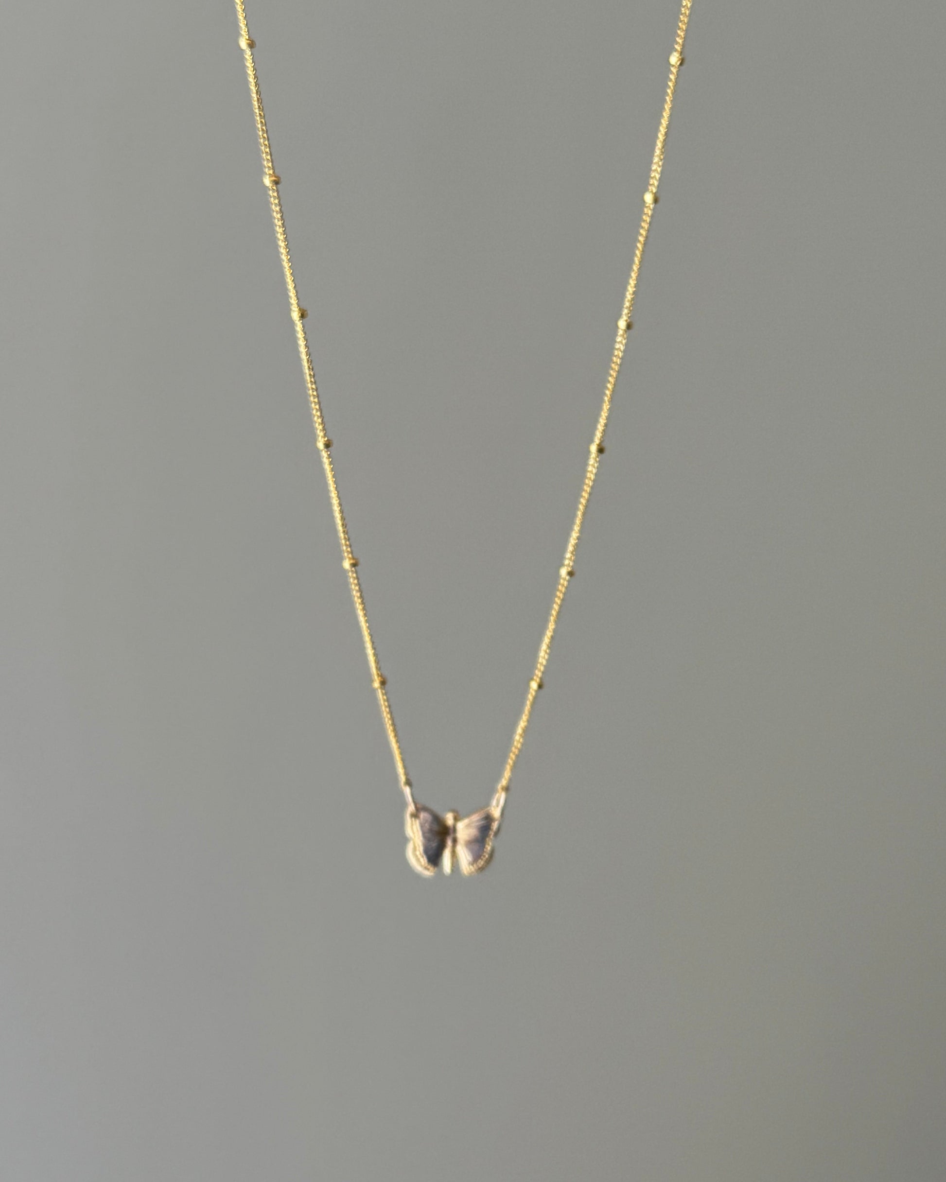 Gold butterfly pendant necklace on a gray background