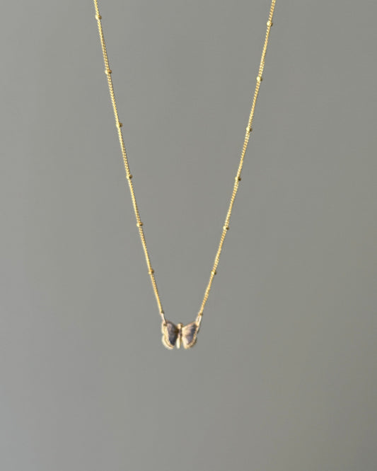 Gold butterfly pendant necklace on a gray background