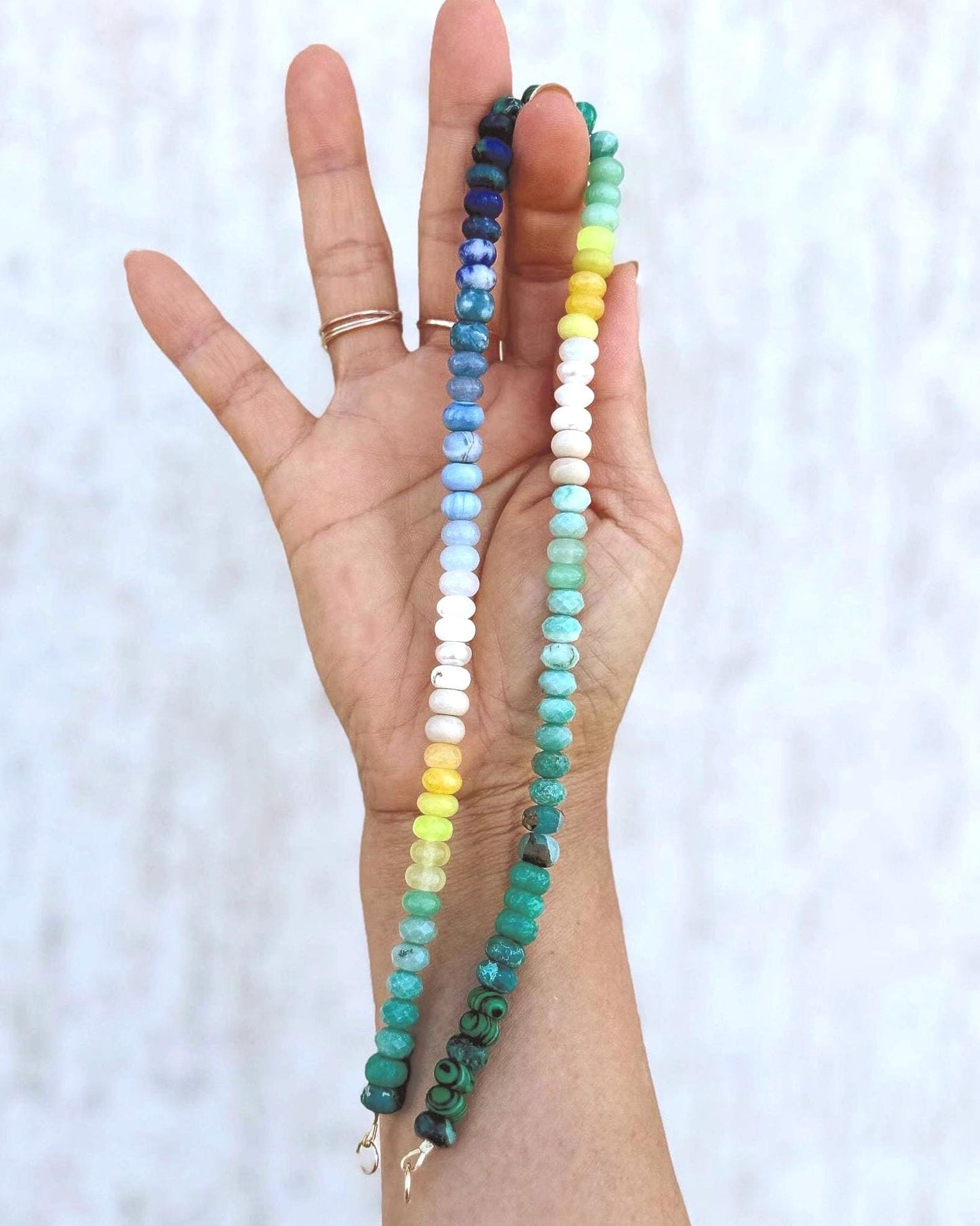 Hand holding a colorful ombré effect beaded gemstone necklace against a white background