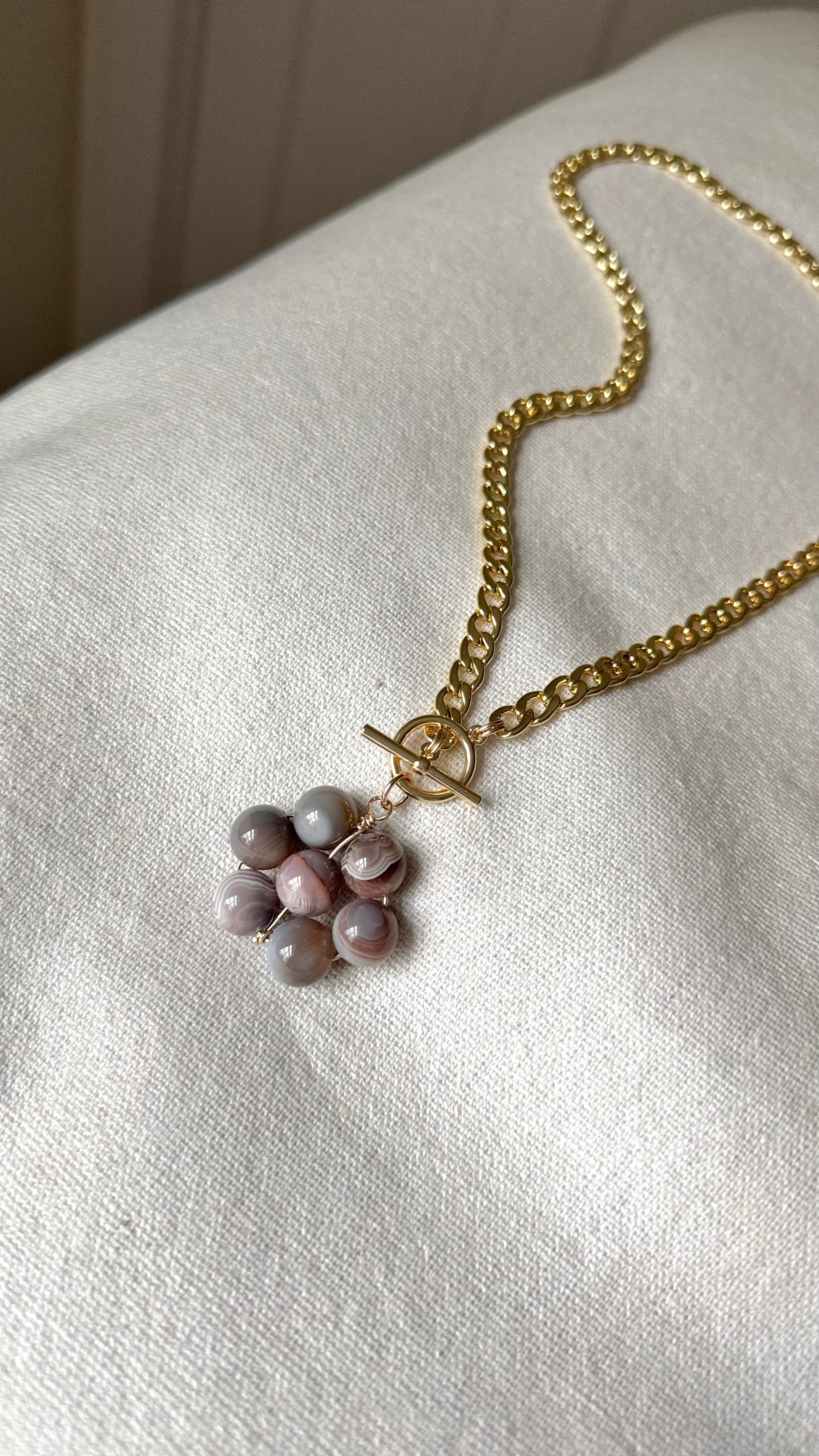 Toggle necklace with a warm gray floral pendant on a light beige surface