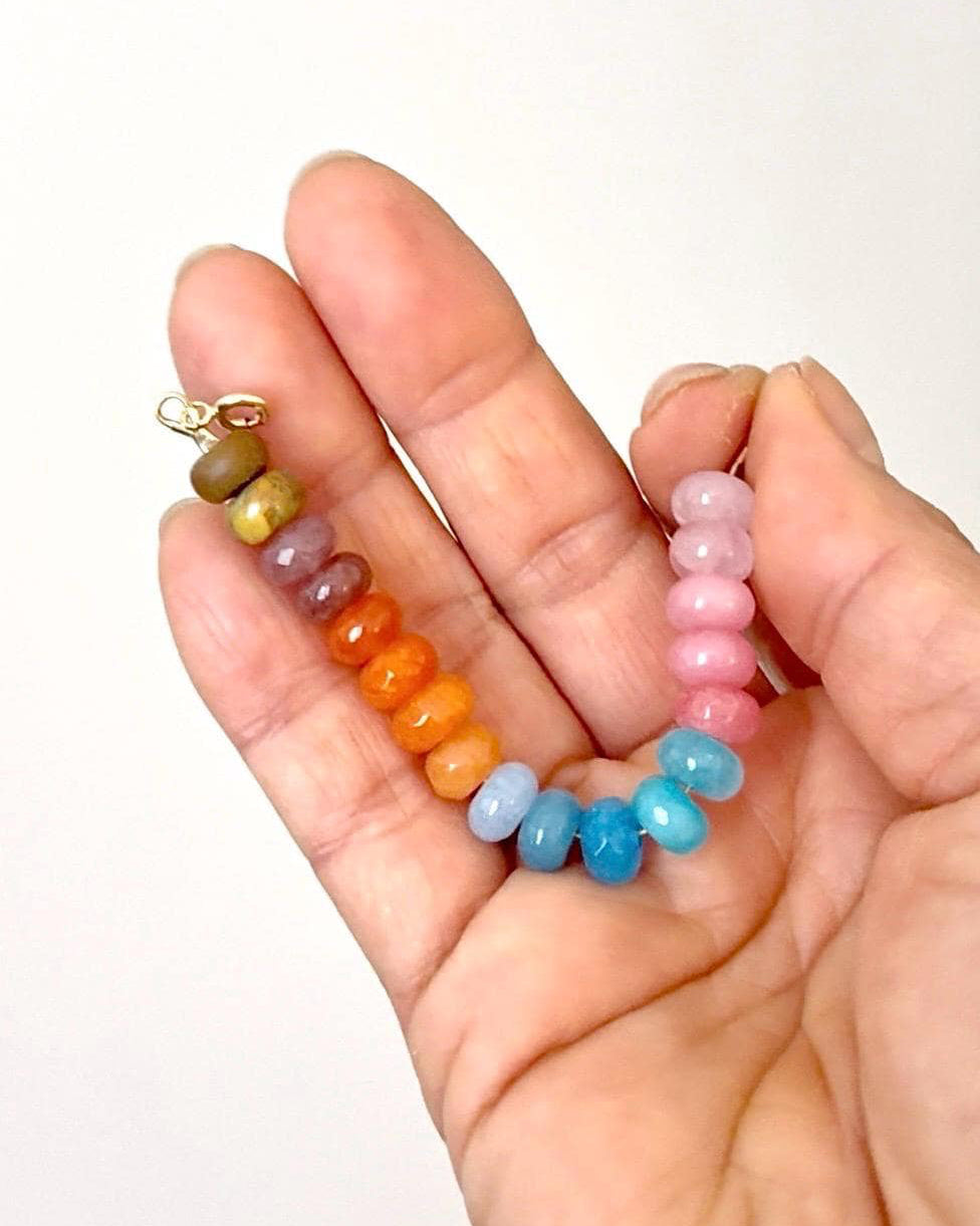 Hand holding colorful ombre effect gemstone beaded bracelets on a white background