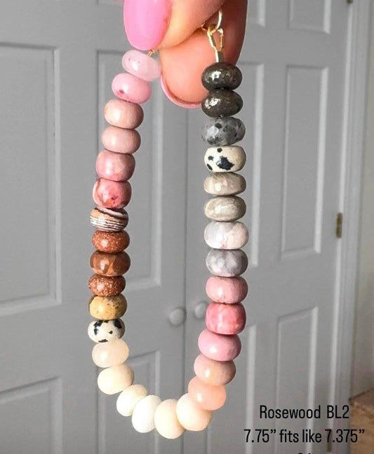 Multi-gemstone beaded bracelet with rose, taupe in ombre effect by a hand against a white door background
